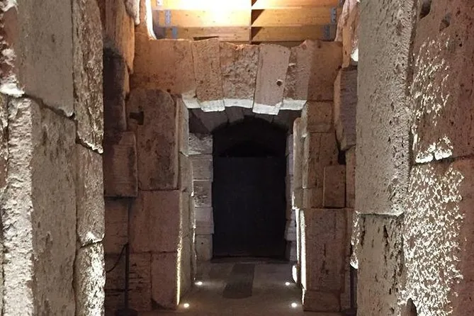 A lit stone doorway deep in the Colosseum underground, between massive blocks of travertine