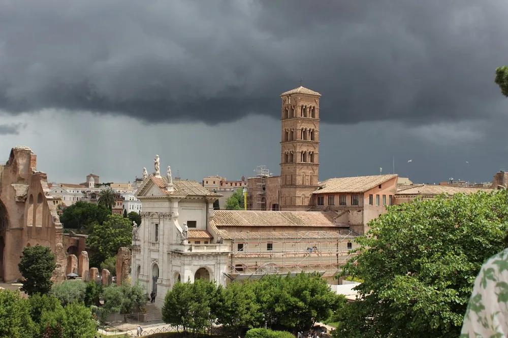 Le Forum romain sous un ciel d'orage sombre, avec un clocher d'église derrière les ruines